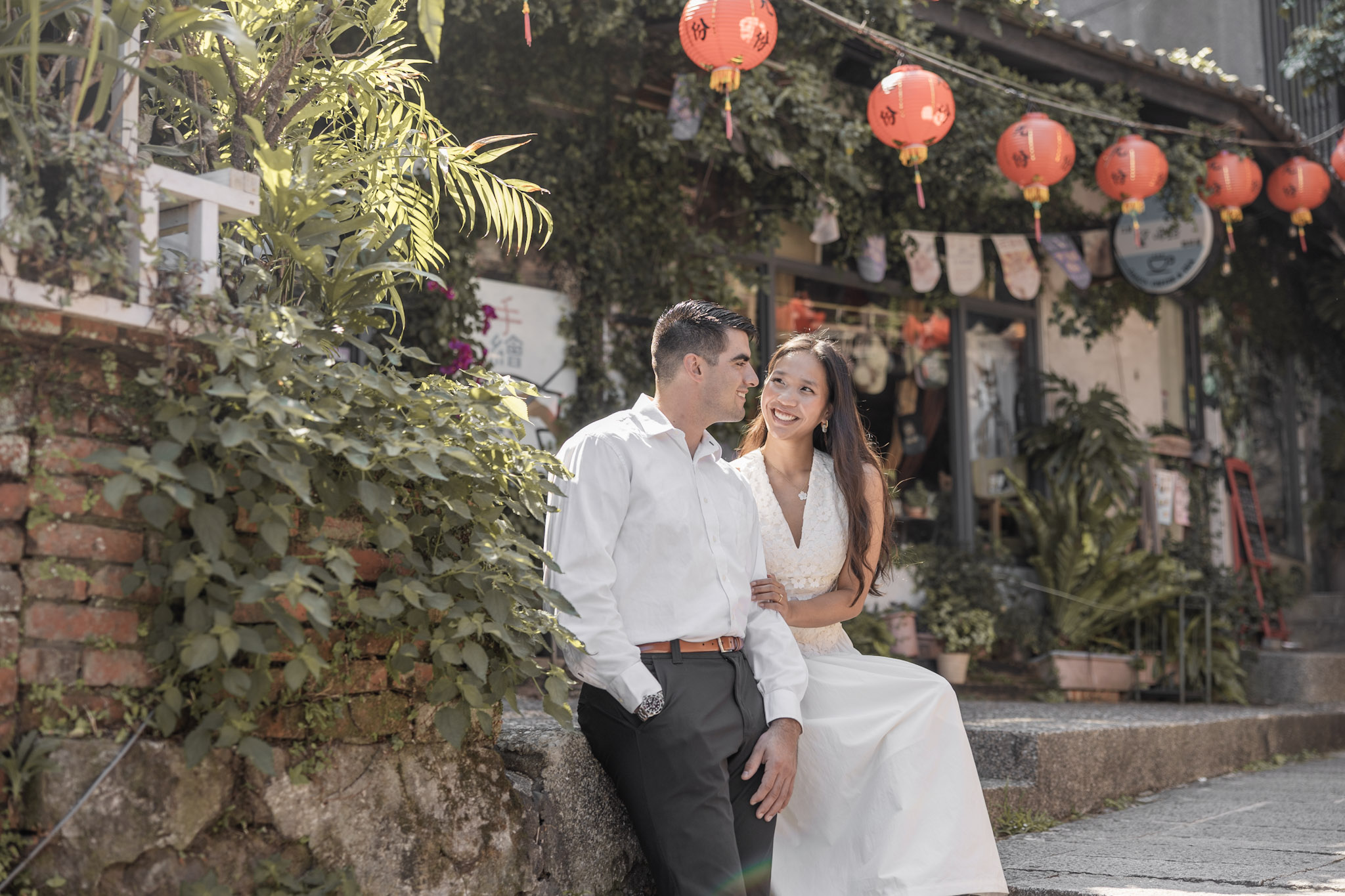 Abigail and Edmund smiling at each other beneath red lanterns in Jiufen, with Abigail’s hand resting on Edmund’s arm.